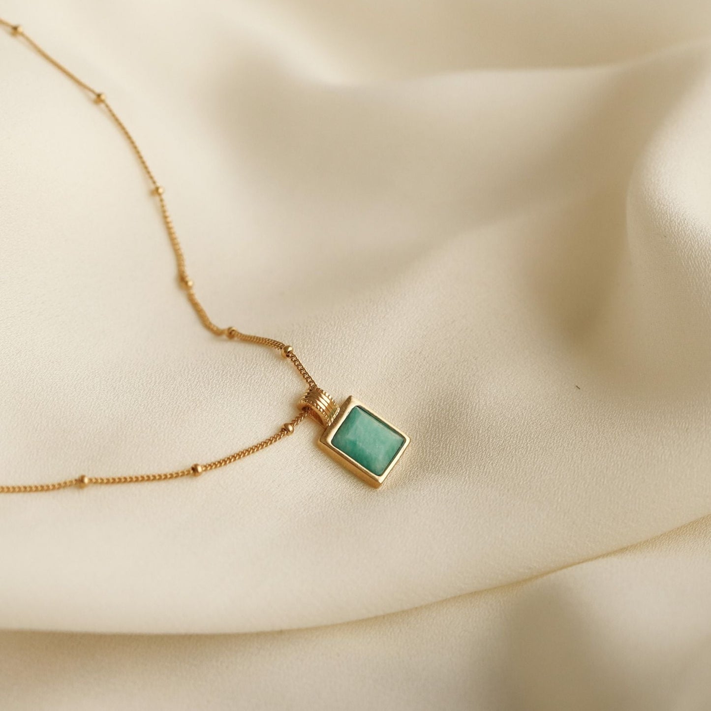 18k gold-plated necklace with a square amazonite blue gemstone pendant on a beige fabric background