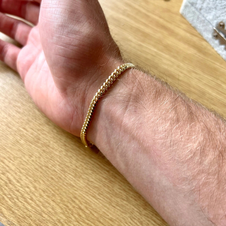 23k Gold-plated Cuban chain bracelet on a wrist against a wooden background