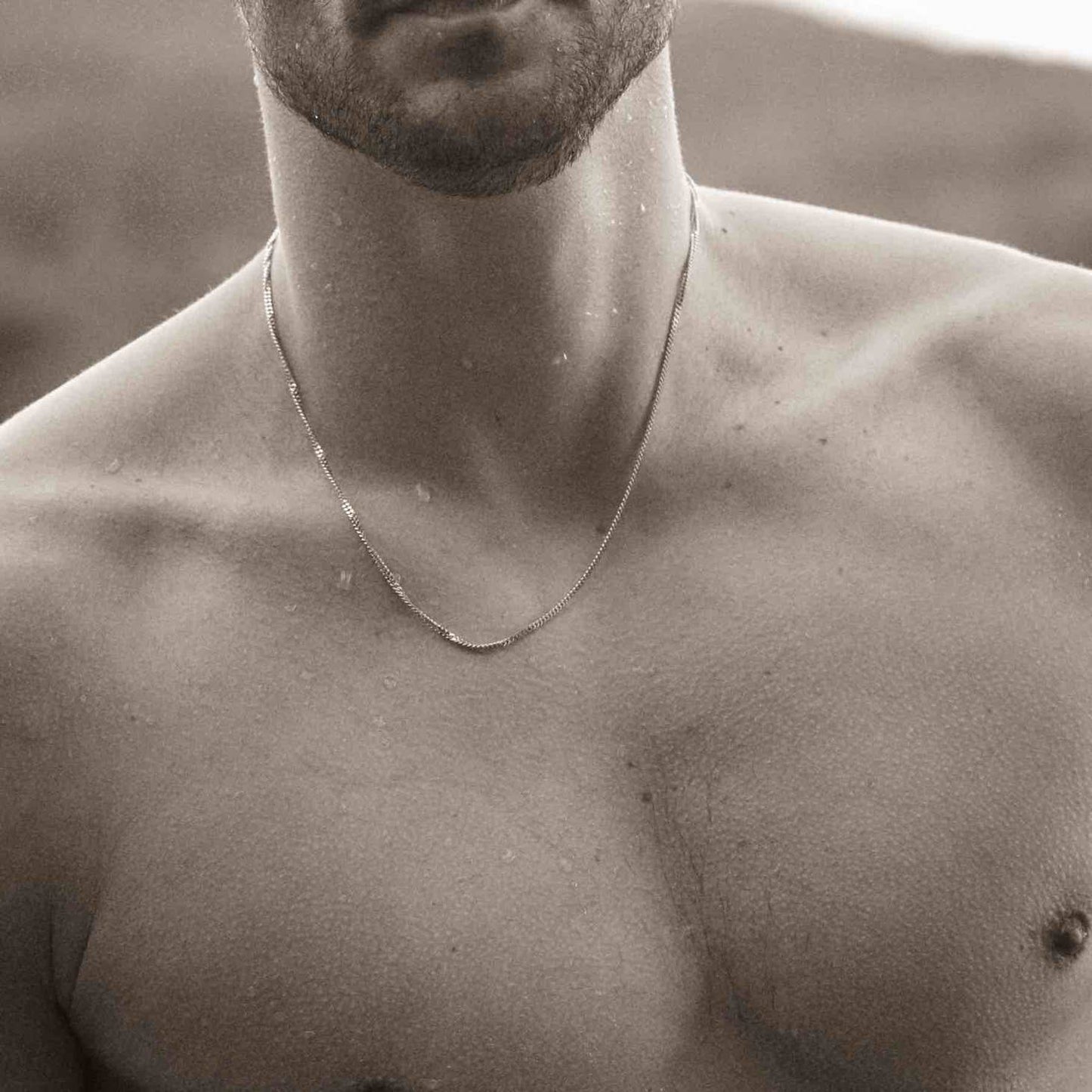 Man modelling an 18k gold plated necklace on the beach