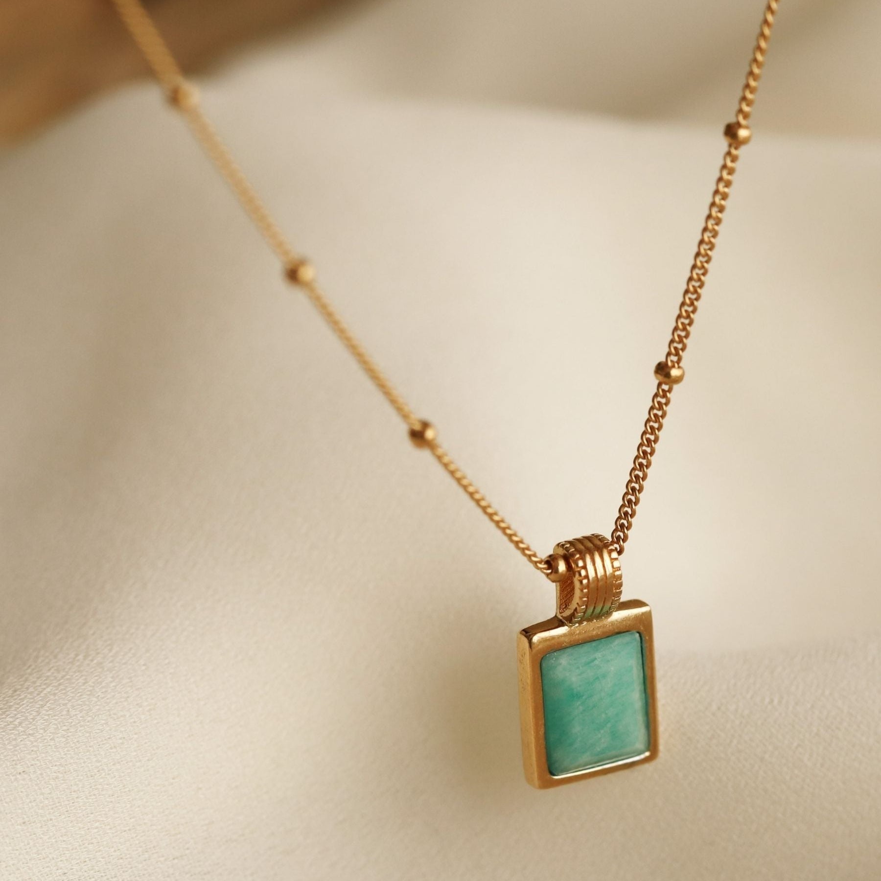 18k gold-plated necklace with a square amazonite blue gemstone pendant on a beige background