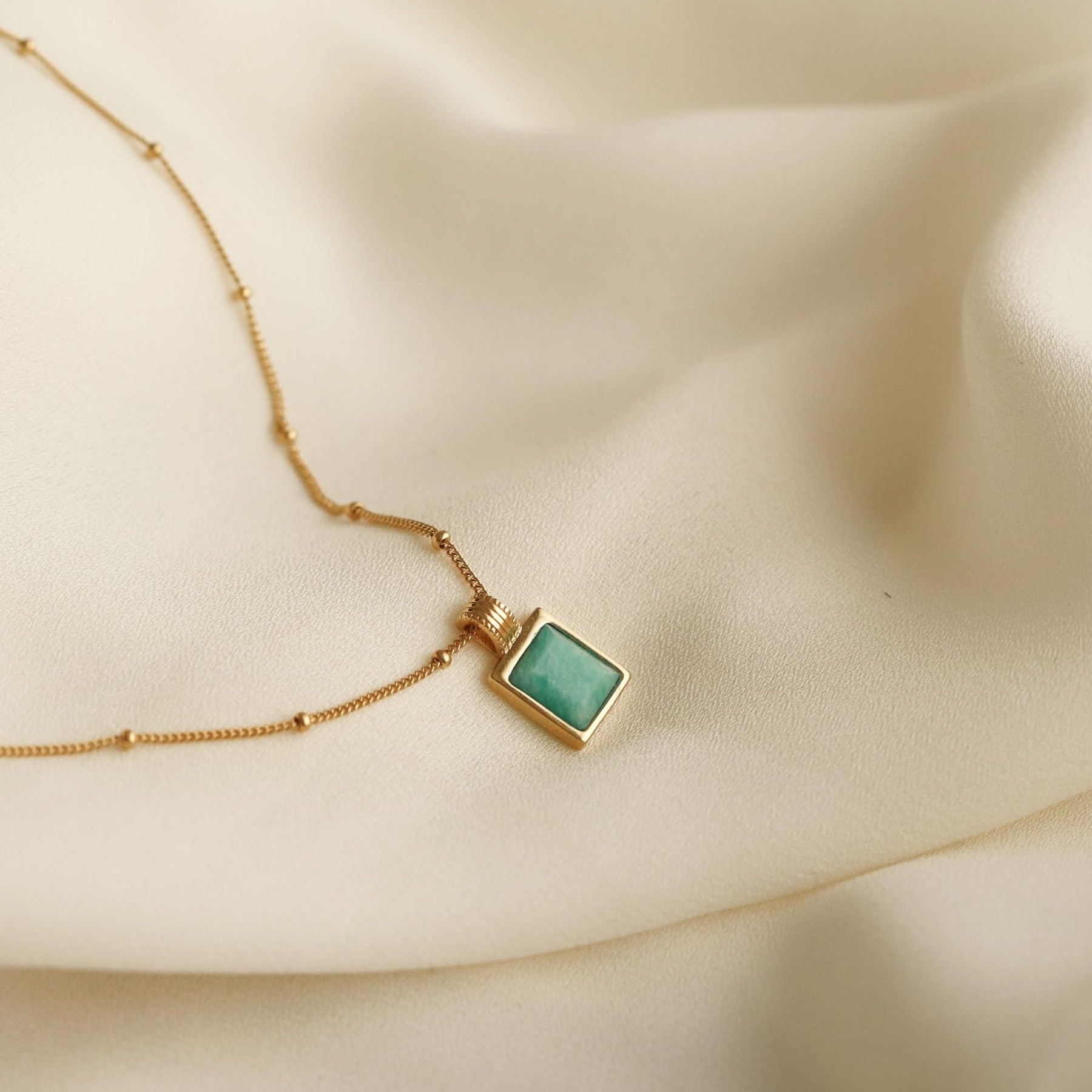 18k gold-plated necklace with a square amazonite blue gemstone pendant on a beige fabric background
