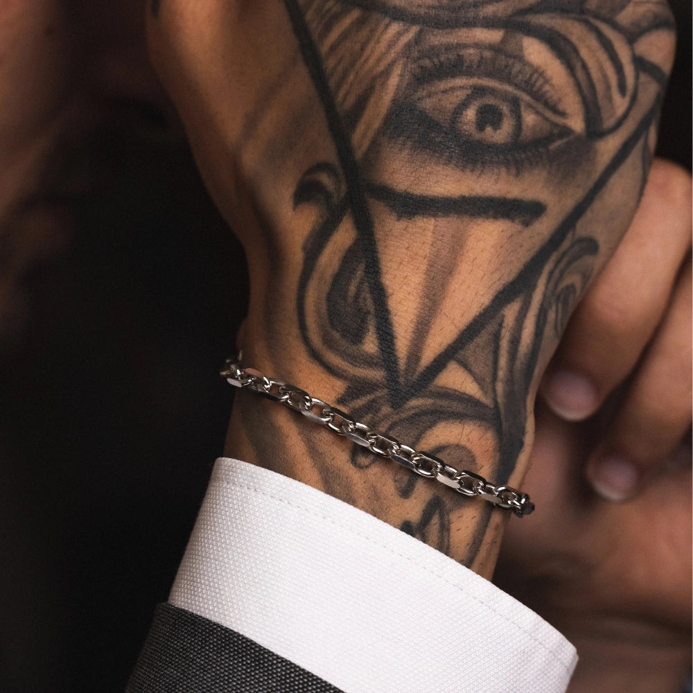 A man's hand with a tattoo wearing a 925 sterling silver rolo chain bracelet.