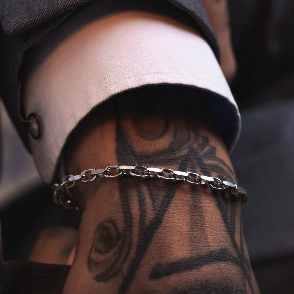 Close-up of a man's arm with tattoos wearing a 925 Sterling silver Rolo chain bracelet.