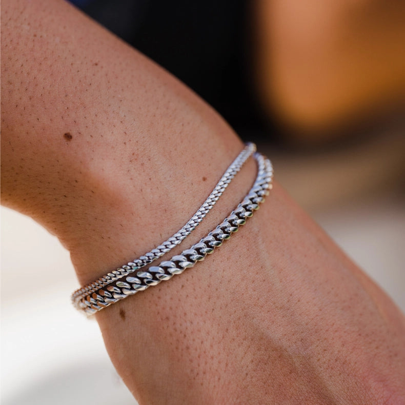 Close-up of a wrist wearing two 925 sterling silver Cuban bracelets on a blurred background