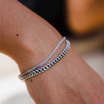Close-up of a wrist wearing two 925 sterling silver Cuban bracelets on a blurred background