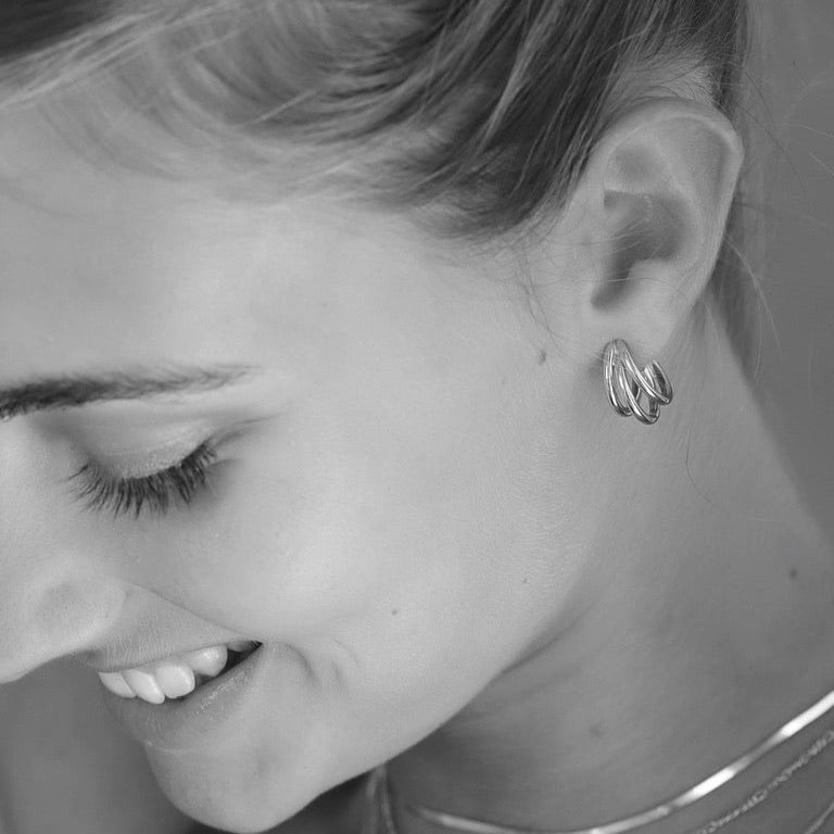 Close up of a woman smiling wearing 925 sterling silver triple hoop earrings with a blurred background