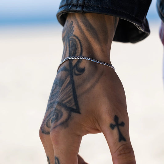 Tattooed man's arm with a 925 sterling silver Cuban chain bracelet on a blurred background