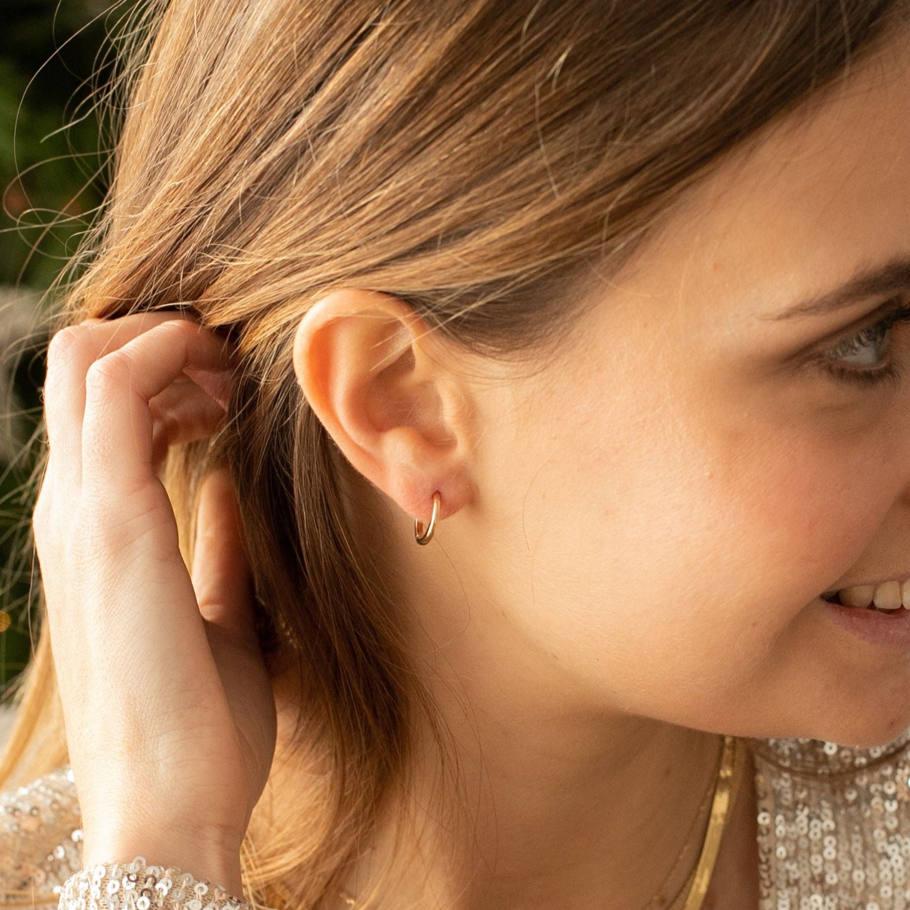 Woman wearing an 18k gold-plated hoop earring and necklace with blurred background